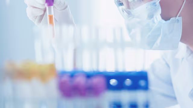 osoba w maseczce z pipetą nad probówkami